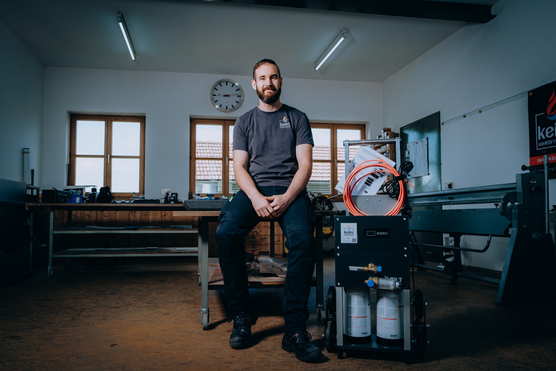 Christoph Keim lächelt, daneben die BWT AQA therm MOVE Spülanlage mit Keim-Banner im Hintergrund.