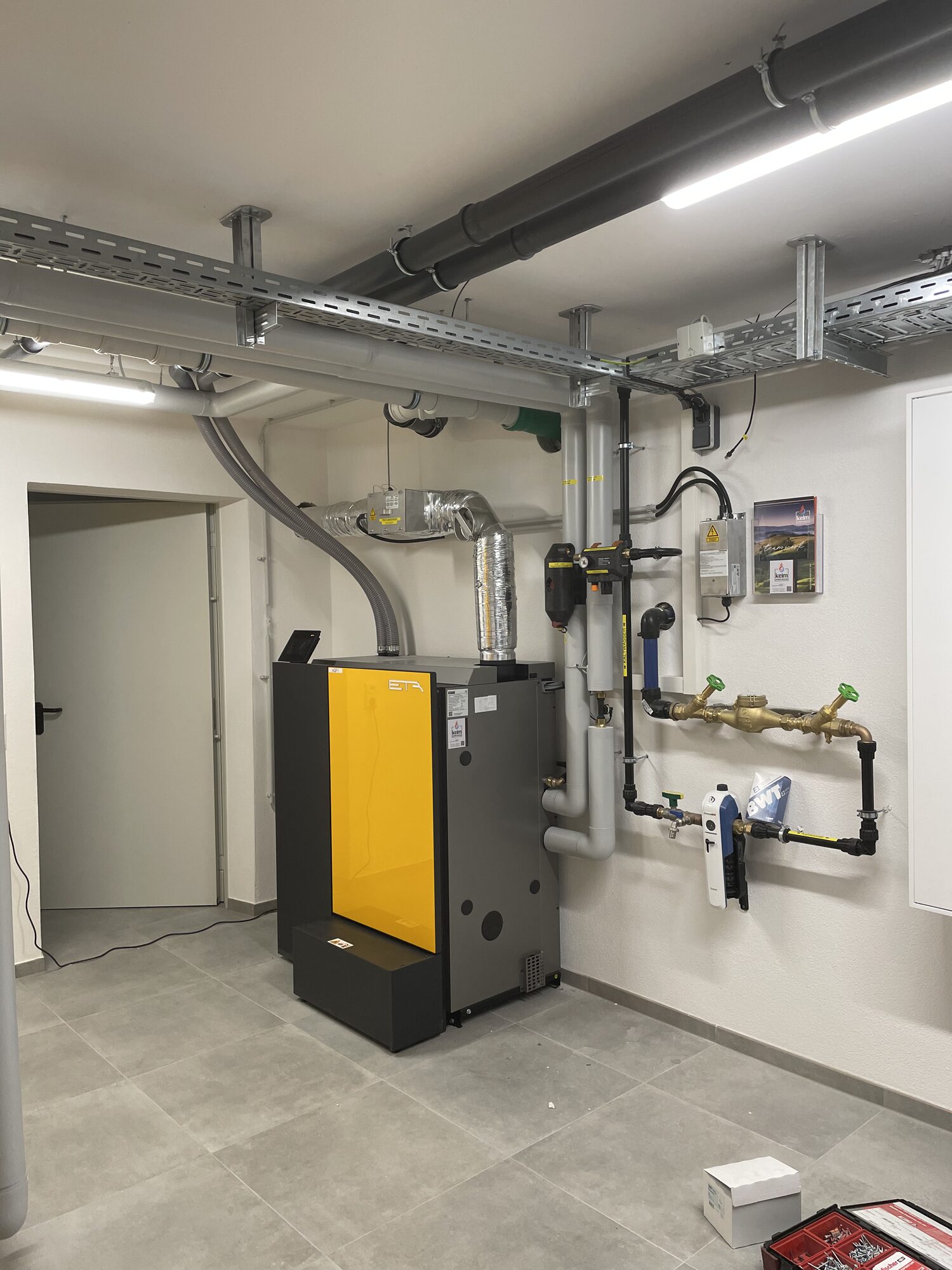 Blick in den Technikraum mit Pelletkessel, Kabeltrassen, Wasserfilter und Systemtrennung
