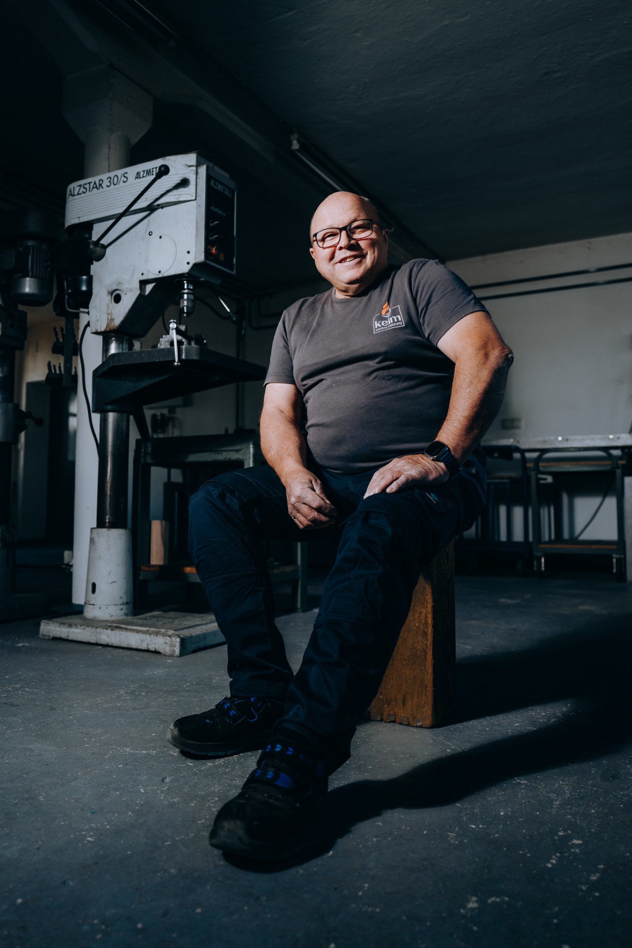 Lächelnder Senior-Chef von keim neben der Ständerbohrmaschine in der Werkstatt.