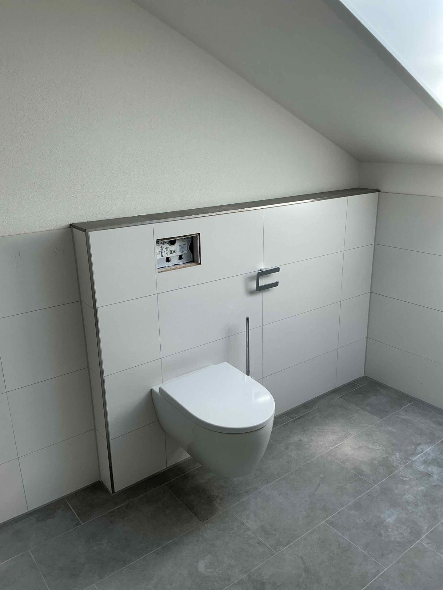 Wand-WC auf Vorwandinstallation mit weißen Fliesen und grauem Bodenbelag