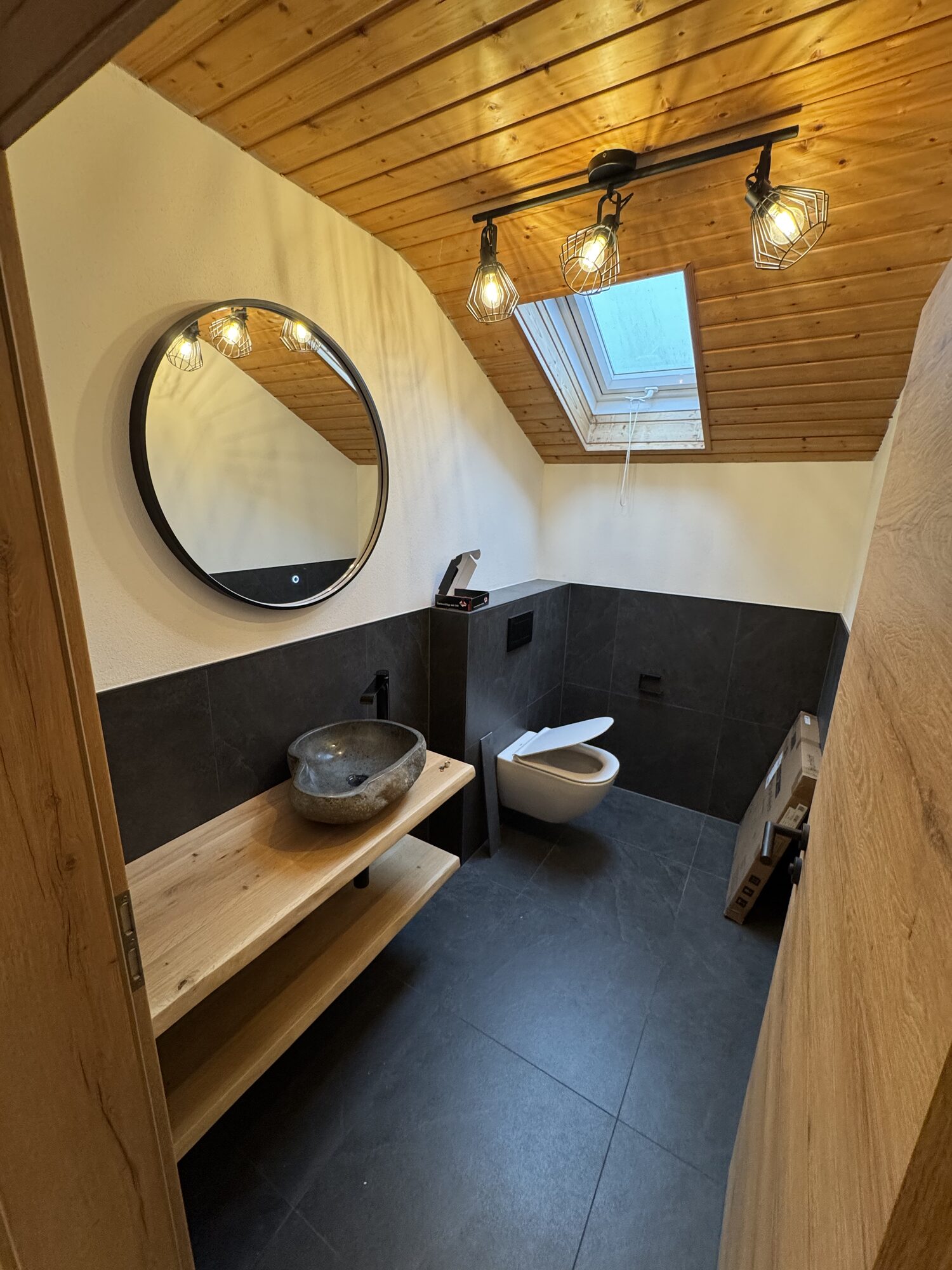 Kleineres Dachgeschossbad mit Holzdecke, rundem Spiegel, Natursteinbecken und Wand-WC