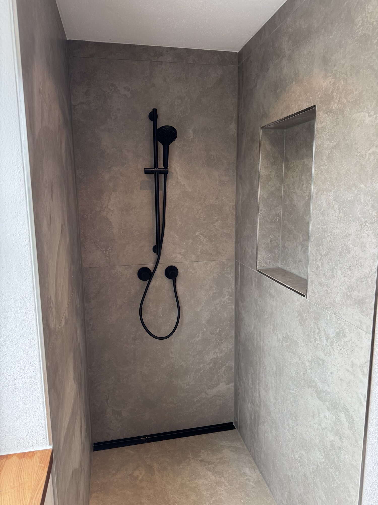 Bodengleiche Dusche in Betonoptik mit schwarzer Unterputzarmatur und Wandnische