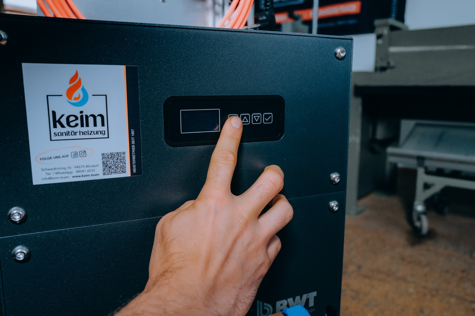 Detailaufnahme: Finger bedient das Display der BWT AQA therm MOVE mit Keim-Aufkleber 'Meisterbetrieb seit 1857'.