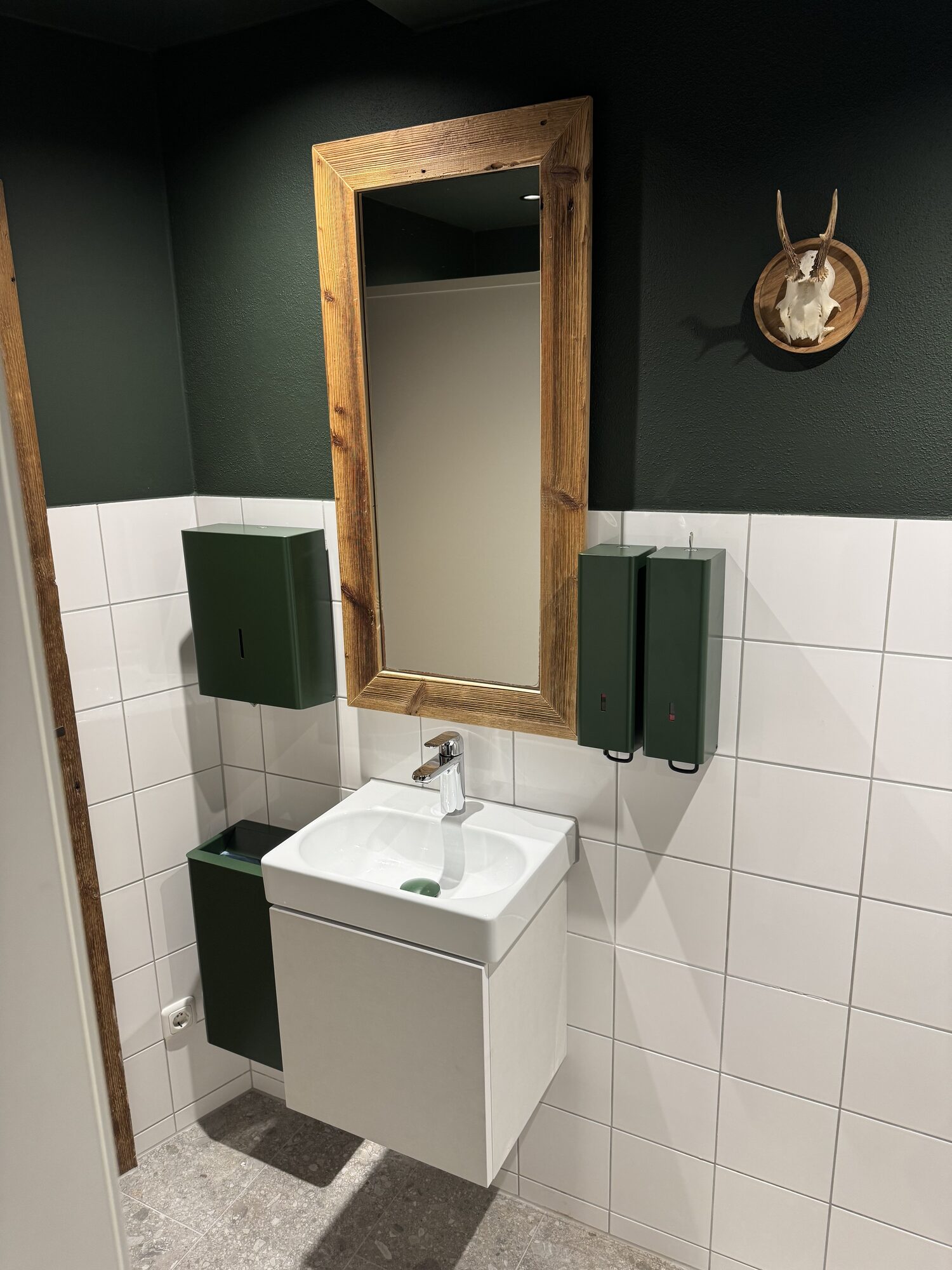 Herren-WC mit grüner Wandfläche und Naturholzelementen