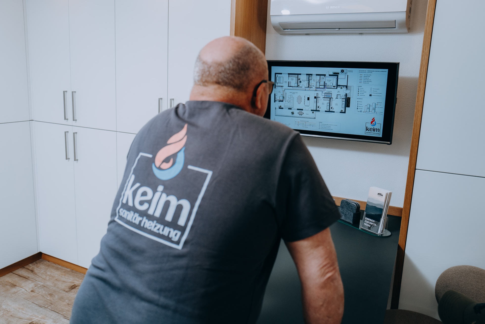 Mitarbeiter im KEIM-Shirt vor dem digitalen Leitungsplan: Trinkwasser, Heizung, Abwasser.