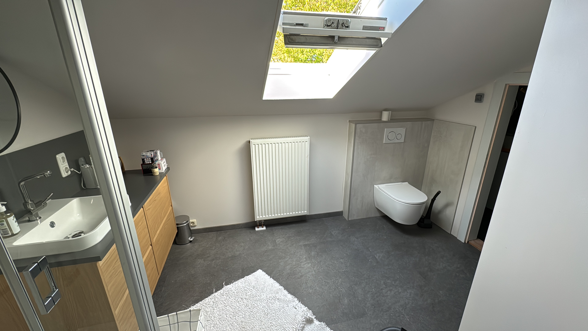 Dachbad mit Wand-WC auf verkleideter Vorwand, Heizkörper und grauem Bodenbelag