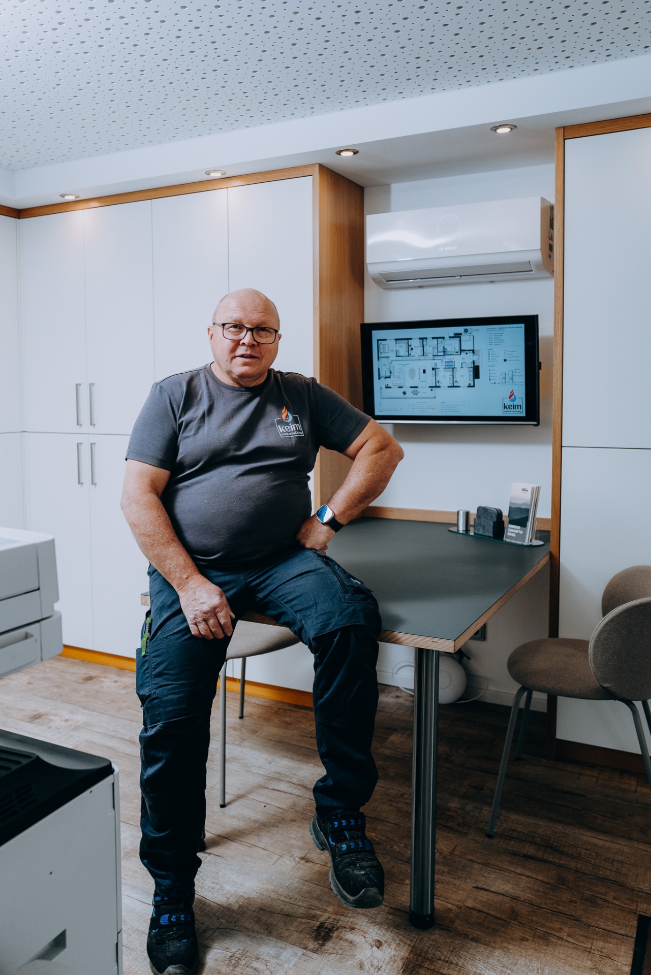 Alfred Keim, Seniorchef, im Showroom vor dem digitalen Leitungsplan und einer Bosch-Klimaanlage.