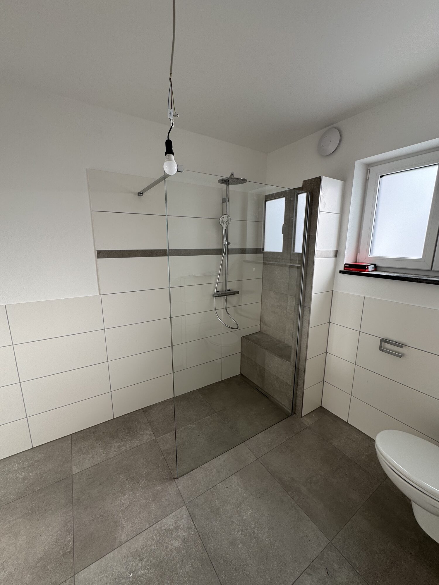 Helles Bad in einer der neuen Wohneinheiten mit bodengleicher Dusche, Glasabtrennung und grauem Fliesenboden