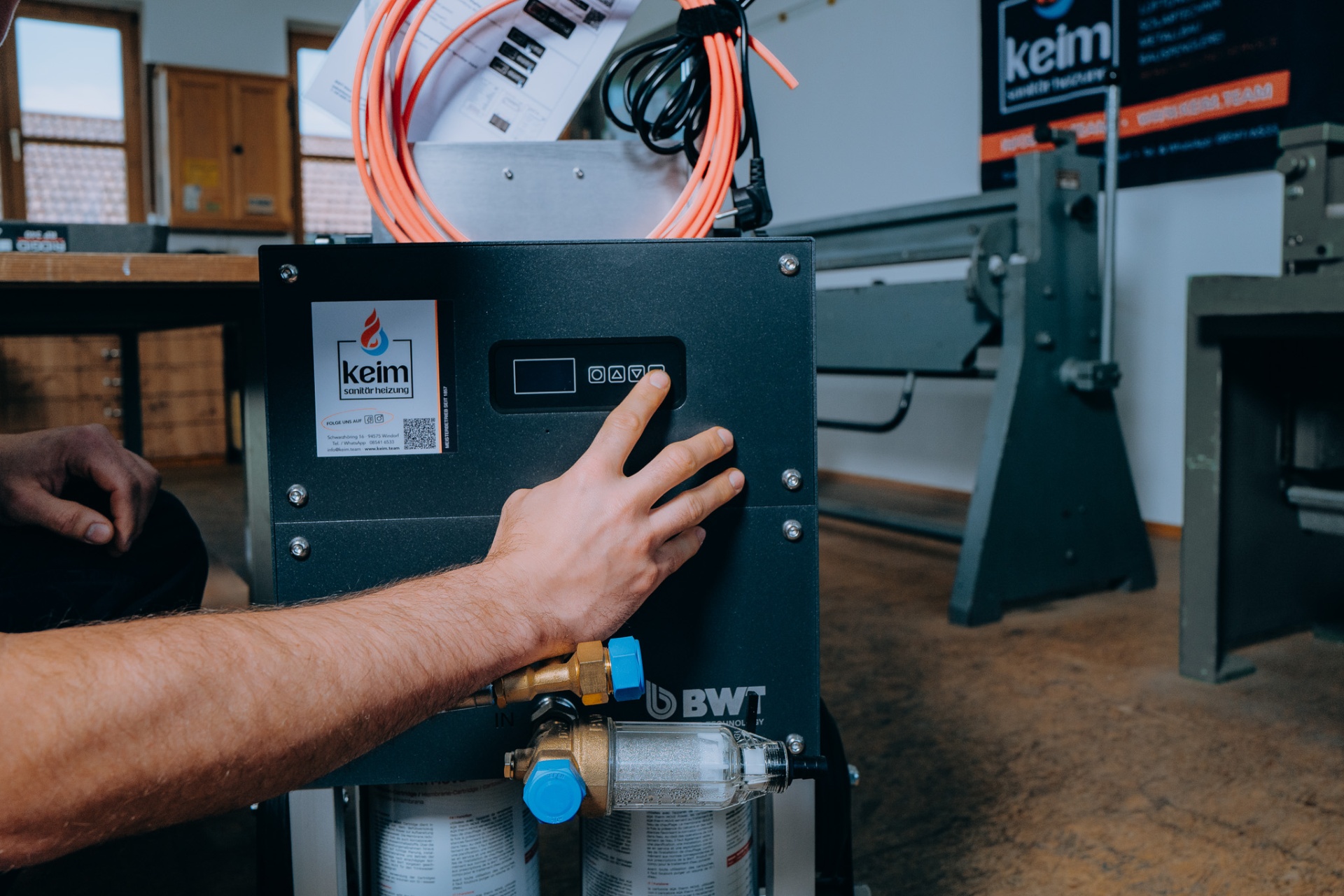 Hand am BWT AQA therm MOVE Bedienfeld — Filter und Anschlüsse im Vordergrund.