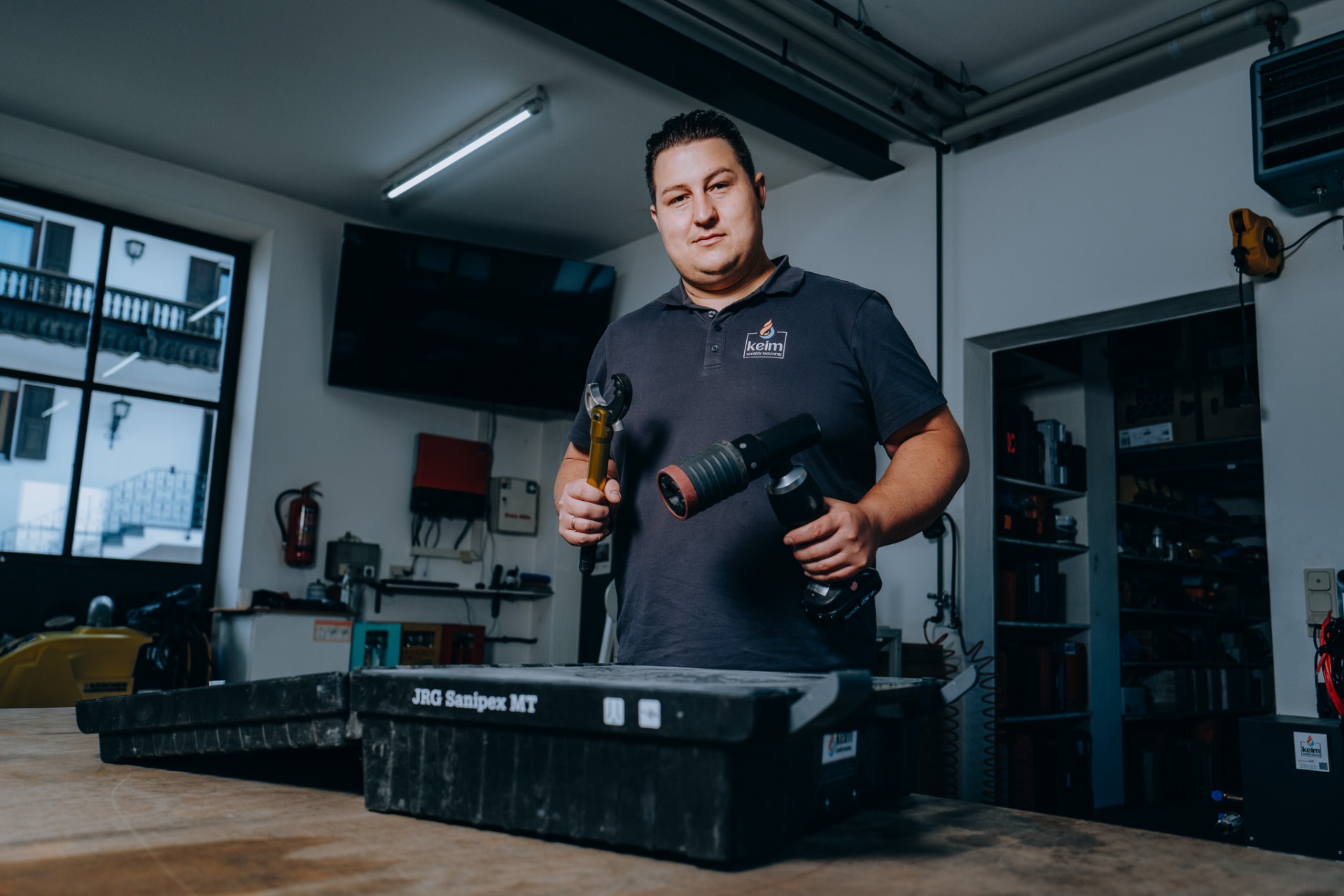 Christoph Keim in der Werkstatt von Keim Sanitär Heizung, mit Pressmaschine und Rohrschneider in den Händen.