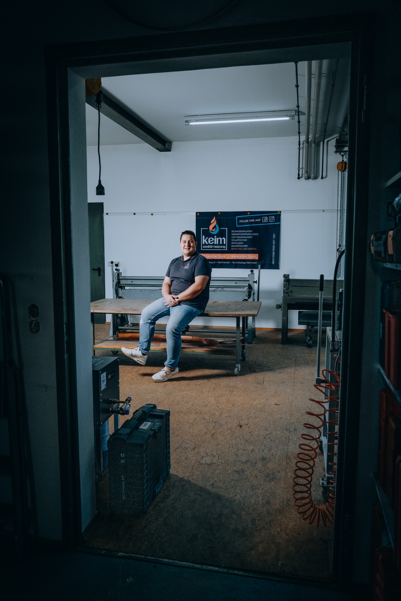 Blick durch die Werkstatttür auf Christoph Keim — Werkzeug und Druckluftspirale im Vordergrund.