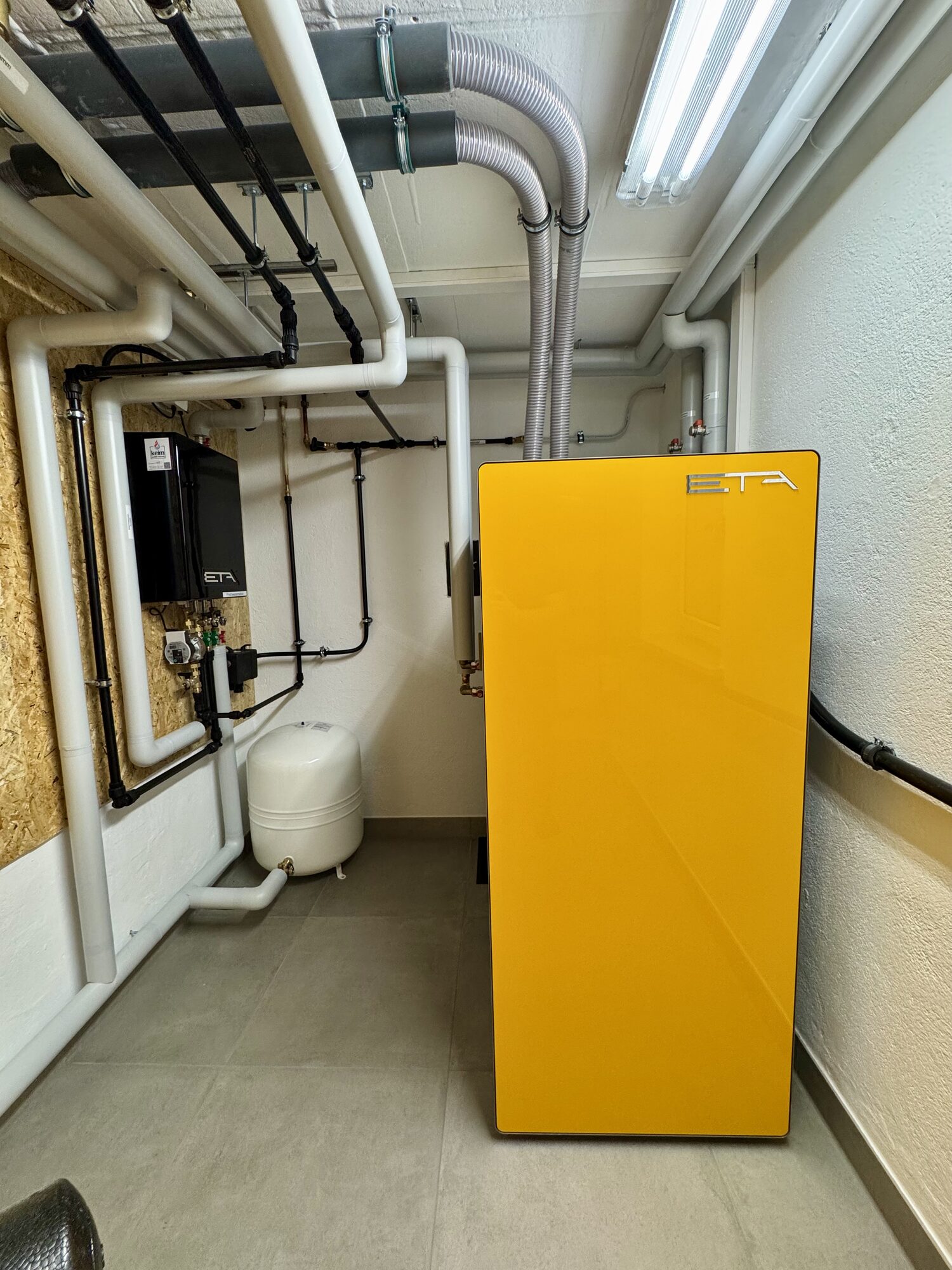 Neuer Pelletkessel im frisch gefliesten Heizraum mit Regelung, Frischwasserstation und sauber verlegten Leitungen