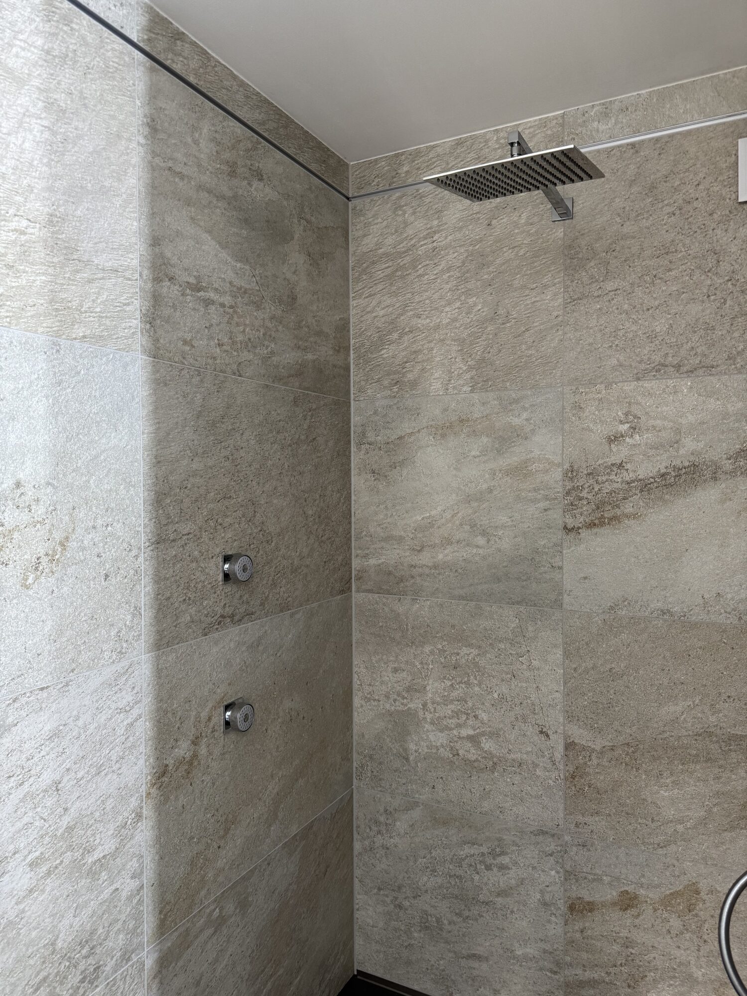 Duschbereich mit Regenbrause und zwei Seitendüsen in Natursteinoptik