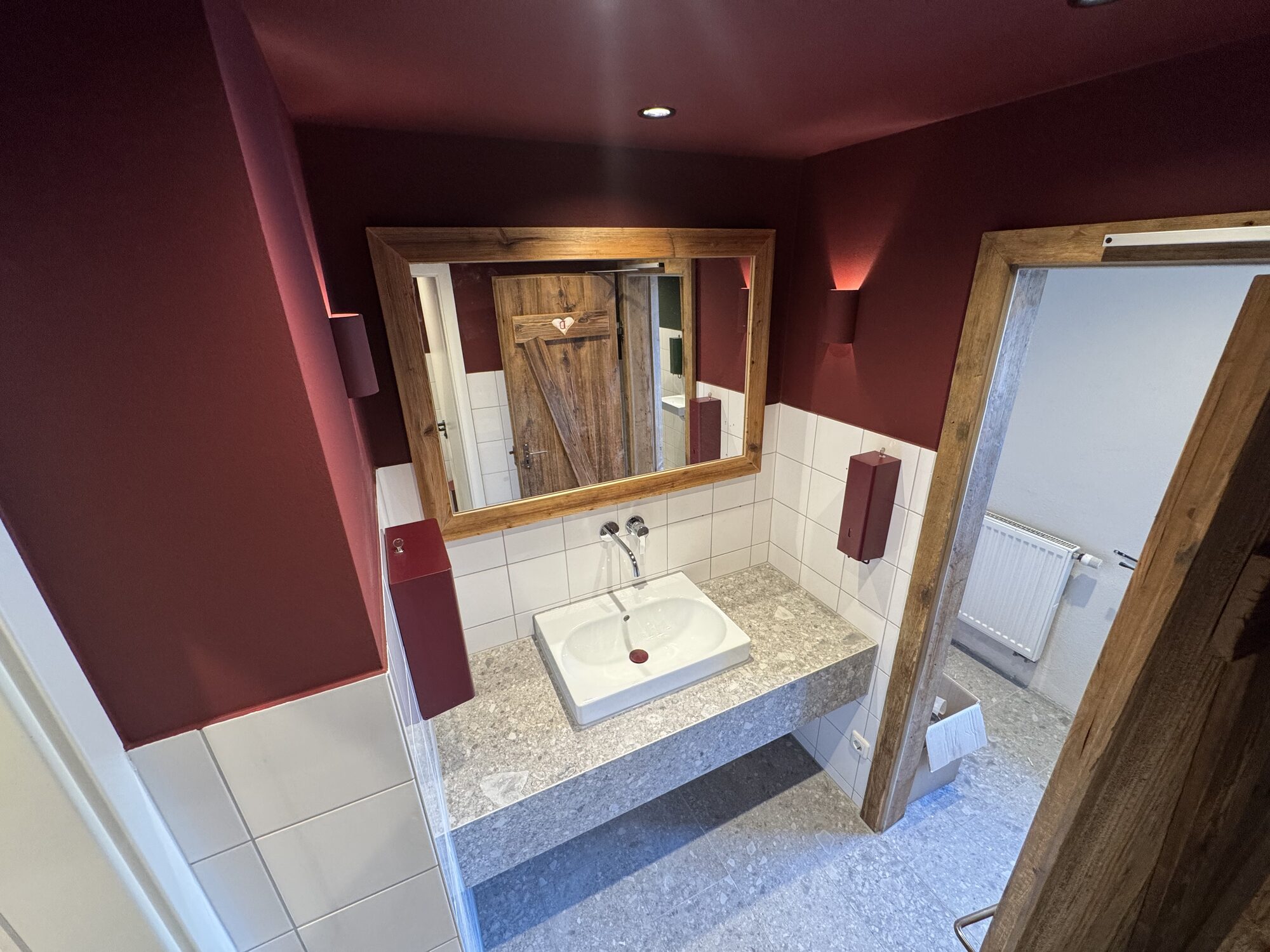 Gäste-WC im Feilmeier's Landleben mit bordeauxroter Wandfläche, Altholzrahmen und Steinwaschtisch