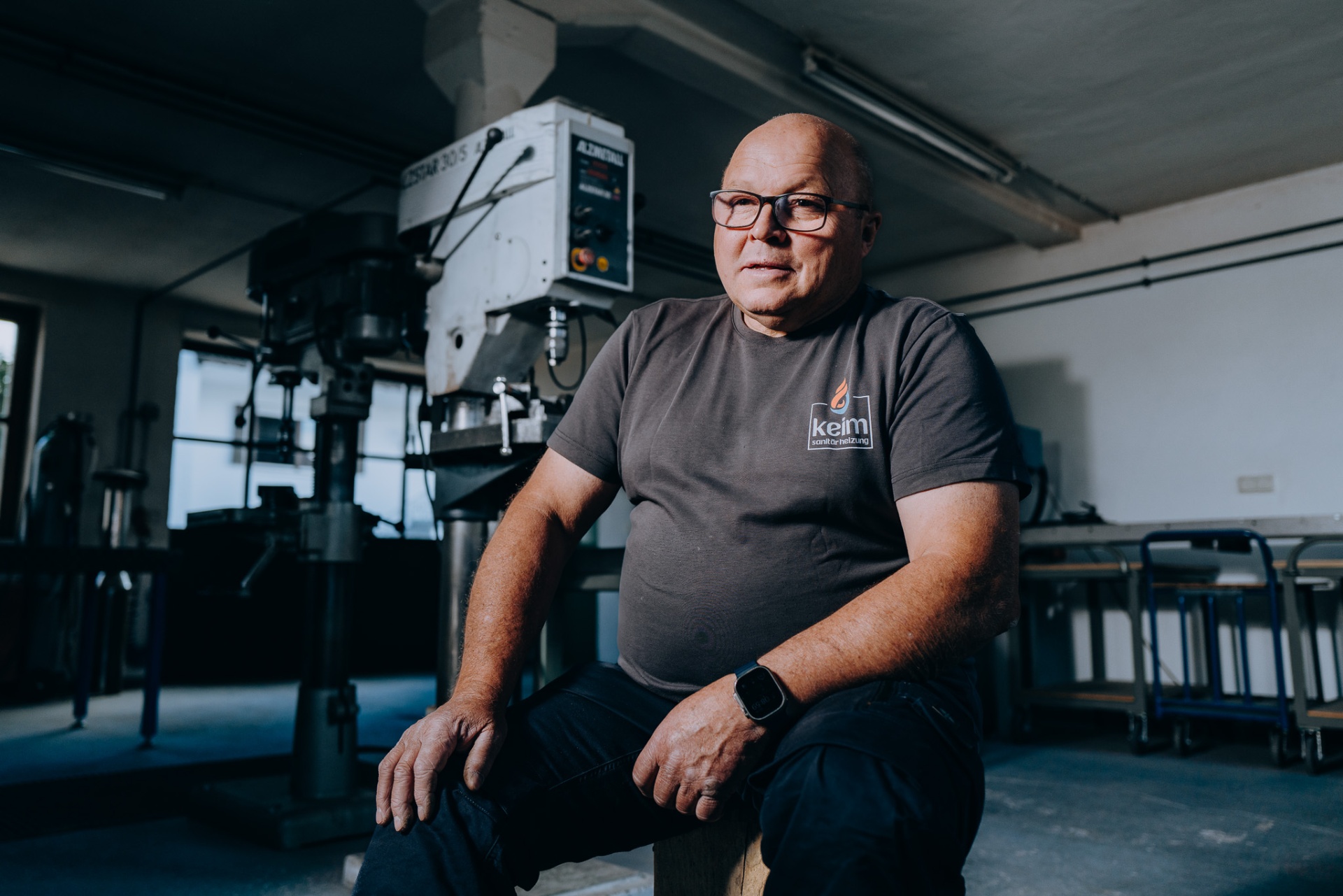 Frontaler Werkstattporträt-Wide des Senior-Chefs vor der Ständerbohrmaschine.