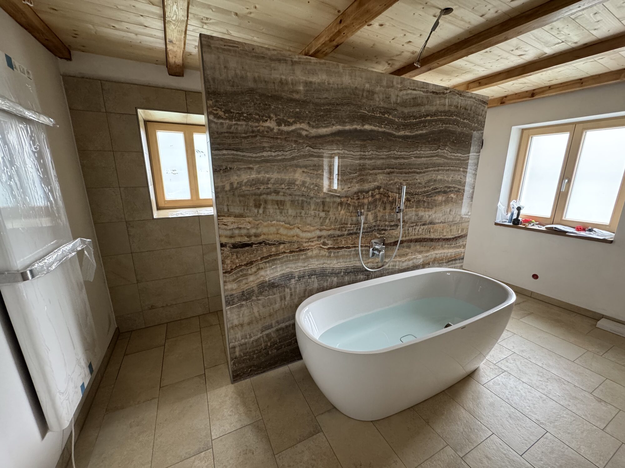 Freistehende Badewanne vor markanter Natursteinwand unter Holzdecke