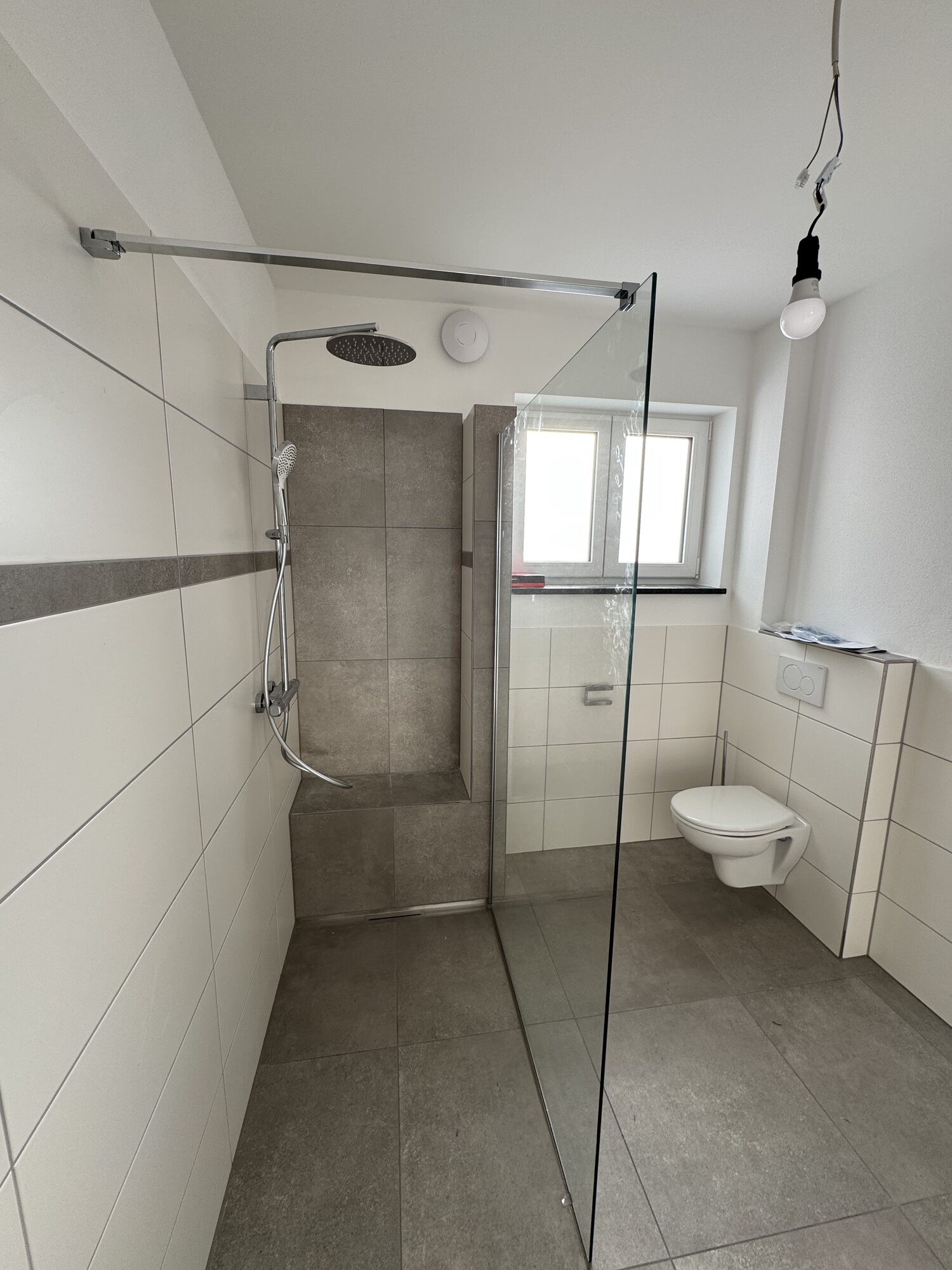 Duschbereich mit Regenbrause, Sitzbank und Wand-WC in einer neuen Wohnung