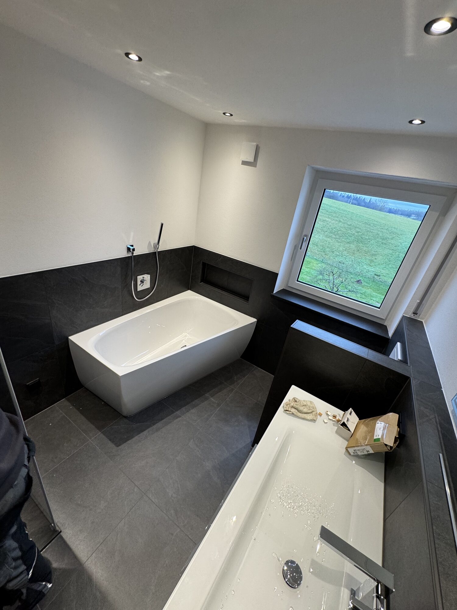Badewanne und bodengleiche Dusche im neu gefliesten Hauptbad in Grau-Weiß